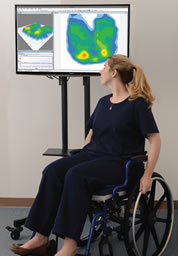 A woman seated in a wheelchair observes a pressure mapping display.